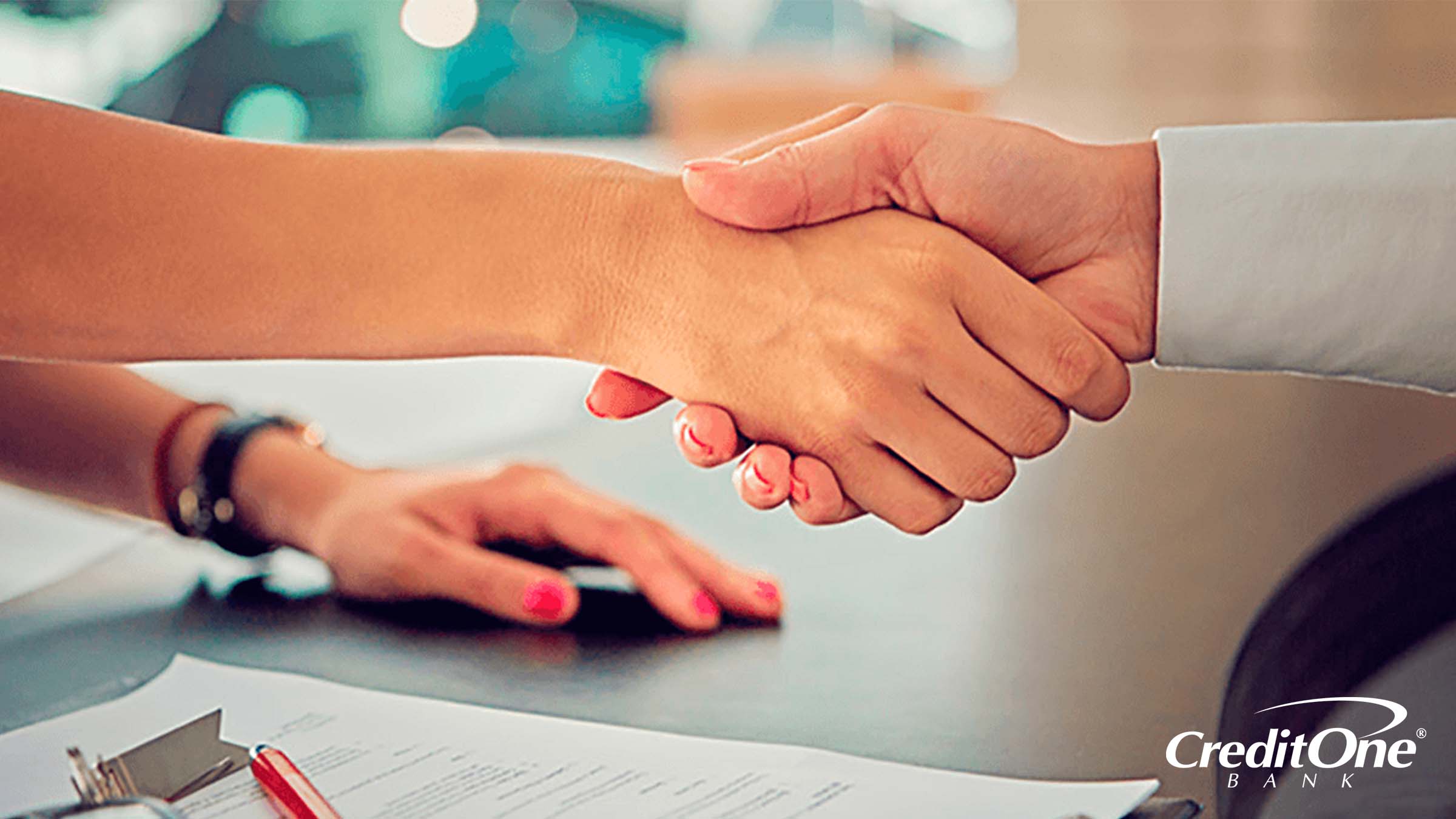 The hands of a man and woman meet for a handshake over some documents, perhaps because the woman’s credit score range helped her get approved for credit.
